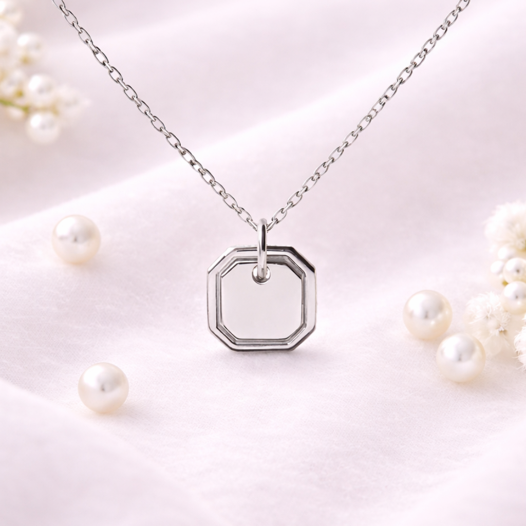 Silver necklace with a hexagonal pendant on a light pink background with pearls.